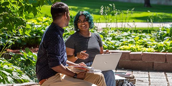 Two students with laptops outdoors talking to one another